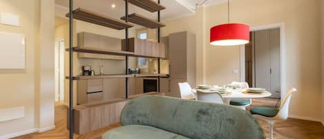 A modern living room with a sofa, dining table, and a kitchen area with wooden shelves.