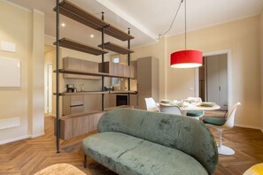 A modern living room with a sofa, dining table, and a kitchen area with wooden shelves.