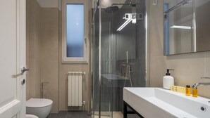 Uma casa de banho moderna com cabine de duche em vidro, sanita e lavatório com produtos de higiene pessoal.