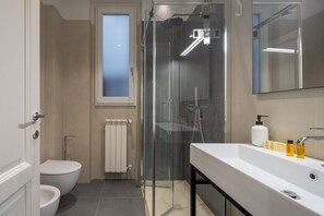 A modern bathroom with a glass-enclosed shower, a toilet, and a sink with toiletries.