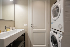 A modern bathroom with a white sink, mirror, and stacked washing machine.