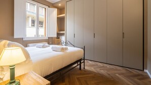 Ein Schlafzimmer mit Bett, Nachttisch mit Lampe, Kleiderschrank und einem Fenster mit Vorhängen.