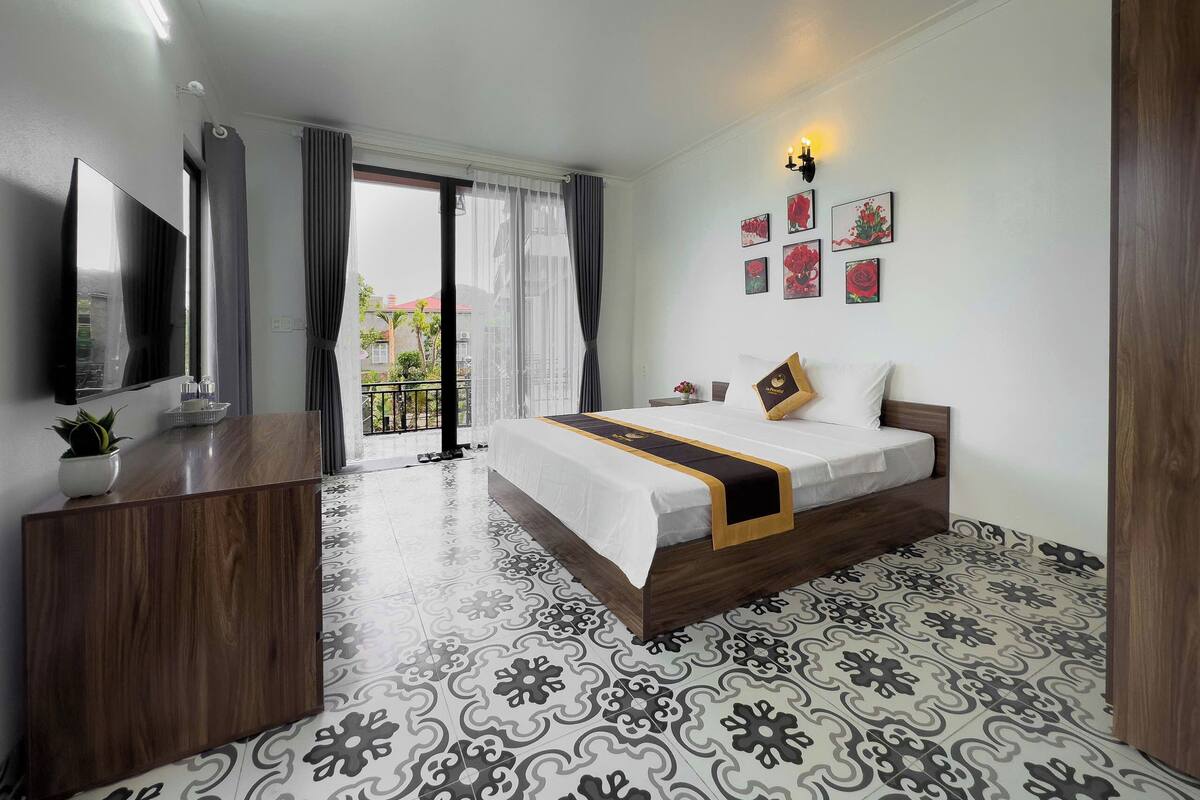 Habitación de hotel con cama, televisor, escritorio y balcón con cortinas.