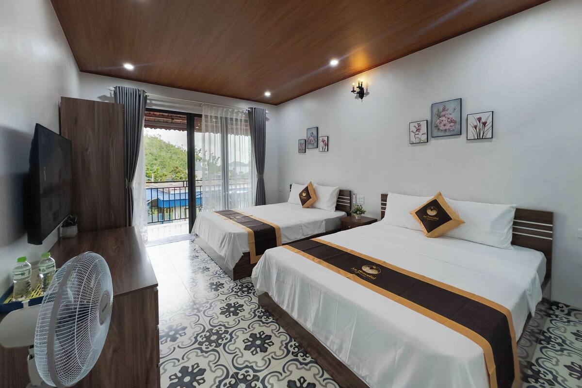 Habitación de hotel con dos camas, televisión, ventilador y balcón con vistas.