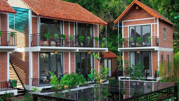 A two-story building with a red-tiled roof, large windows, and balconies with plants. - An Peaceful Homestay (Hai Phong)