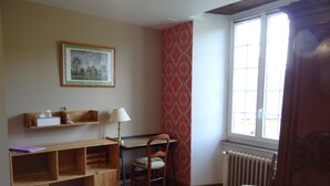 A room with a wooden desk, chair, and shelves. There is a window with a view, a radiator, and a patterned rug.