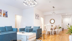 En moderne stue med blå sofaarrangement, et hvidt sofabord og et spiseområde med hvide stole og et rundt bord.