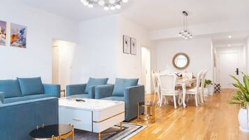 A modern living room with a blue sofa set, a white coffee table, and a dining area with white chairs and a round table.