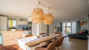 Un espacio habitable moderno con una mesa de comedor de madera, sillas de cuero marrón, un sofá y una zona de cocina con ventana.