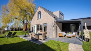 Una casa moderna con un patio que incluye mobiliario exterior y una parrilla.