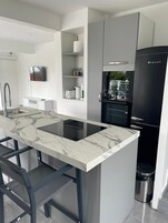 A modern kitchen with a marble countertop, integrated appliances, and a black refrigerator.