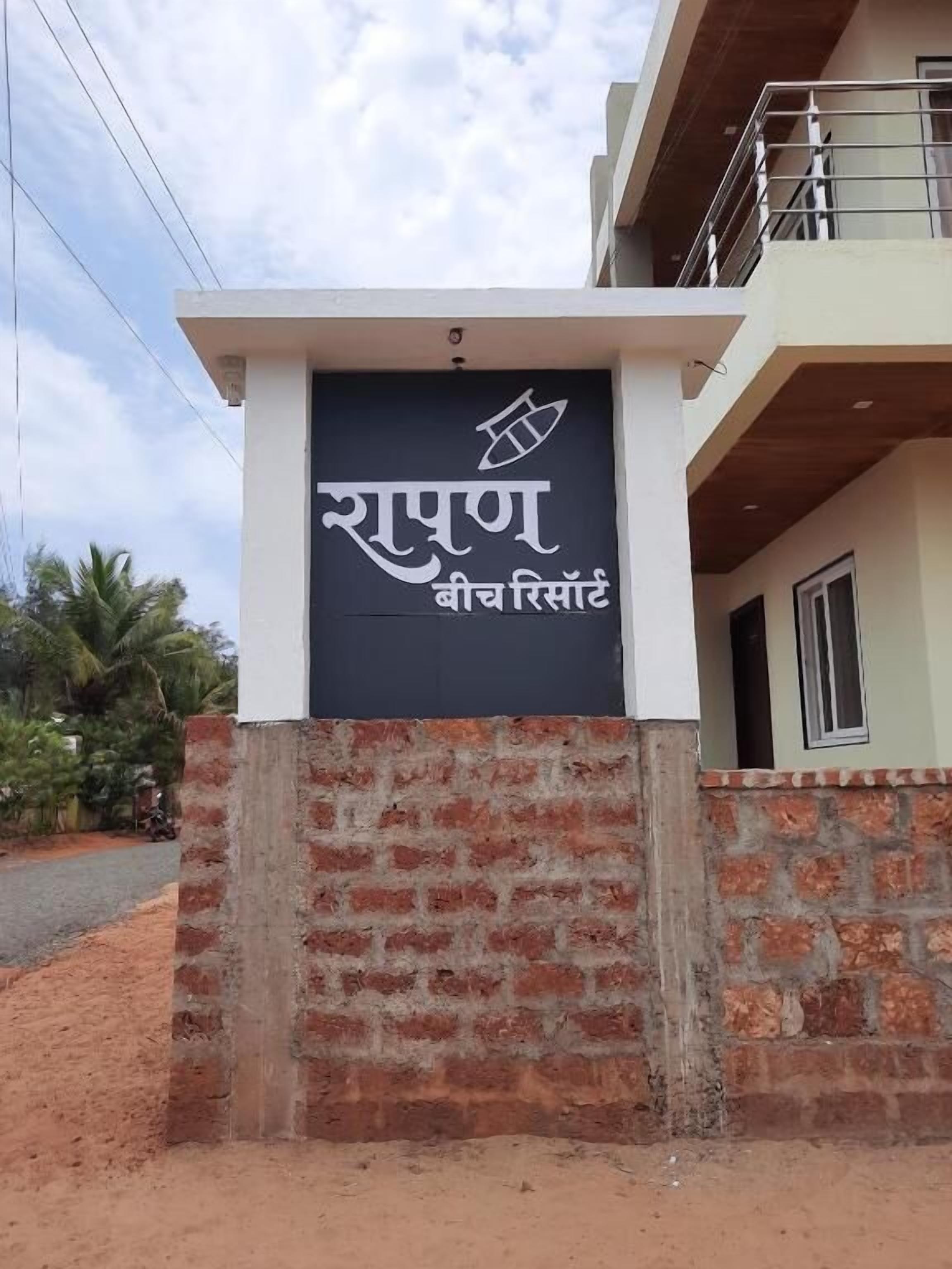 A sign for a hotel with a logo and name in a foreign script, a brick wall, and a building with a balcony.