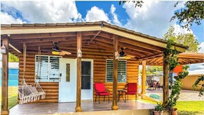 A log cabin with a covered porch, a hammock, red chairs, and a pool area. - Cabaña Del Sol-Small Cabin Near The Best Beaches in Cabo Rojo with generator (Cabo Rojo)