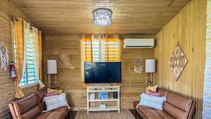 A cozy living room with two leather sofas, a flat-screen TV, and a wooden ceiling. - Cabaña Del Sol-Small Cabin Near The Best Beaches in Cabo Rojo with generator (Cabo Rojo)