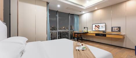 A hotel room with a bed, a desk with a chair, a television, and a city view through large windows.