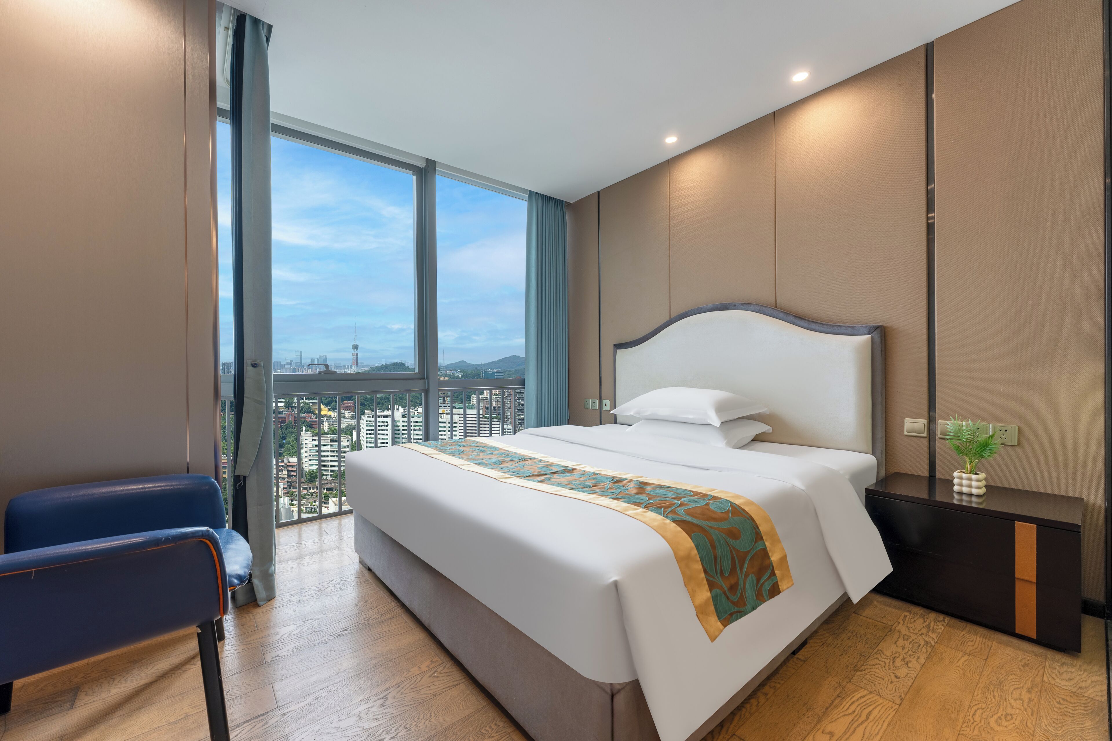 Habitación de hotel moderna con una cama grande, una mesita de noche, una silla y vistas de la ciudad a través de amplios ventanales.