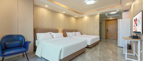 A hotel room with two beds, a blue chair, a small table, and a door leading to another room.