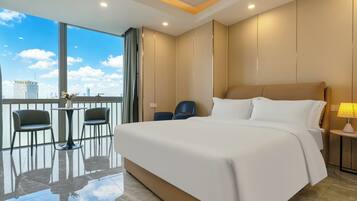 A hotel room with a large bed, two chairs, a small table, and a view of the city skyline.