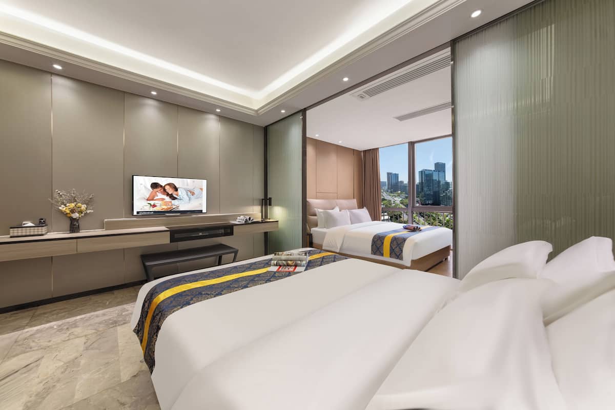 Quarto de hotel moderno com uma cama grande, uma escrivaninha, uma televisão e vista para a cidade.