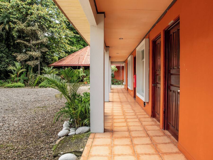 Uma galeria coberta com piso de azulejos que conduz a um edifício com paredes laranja e portas de madeira.