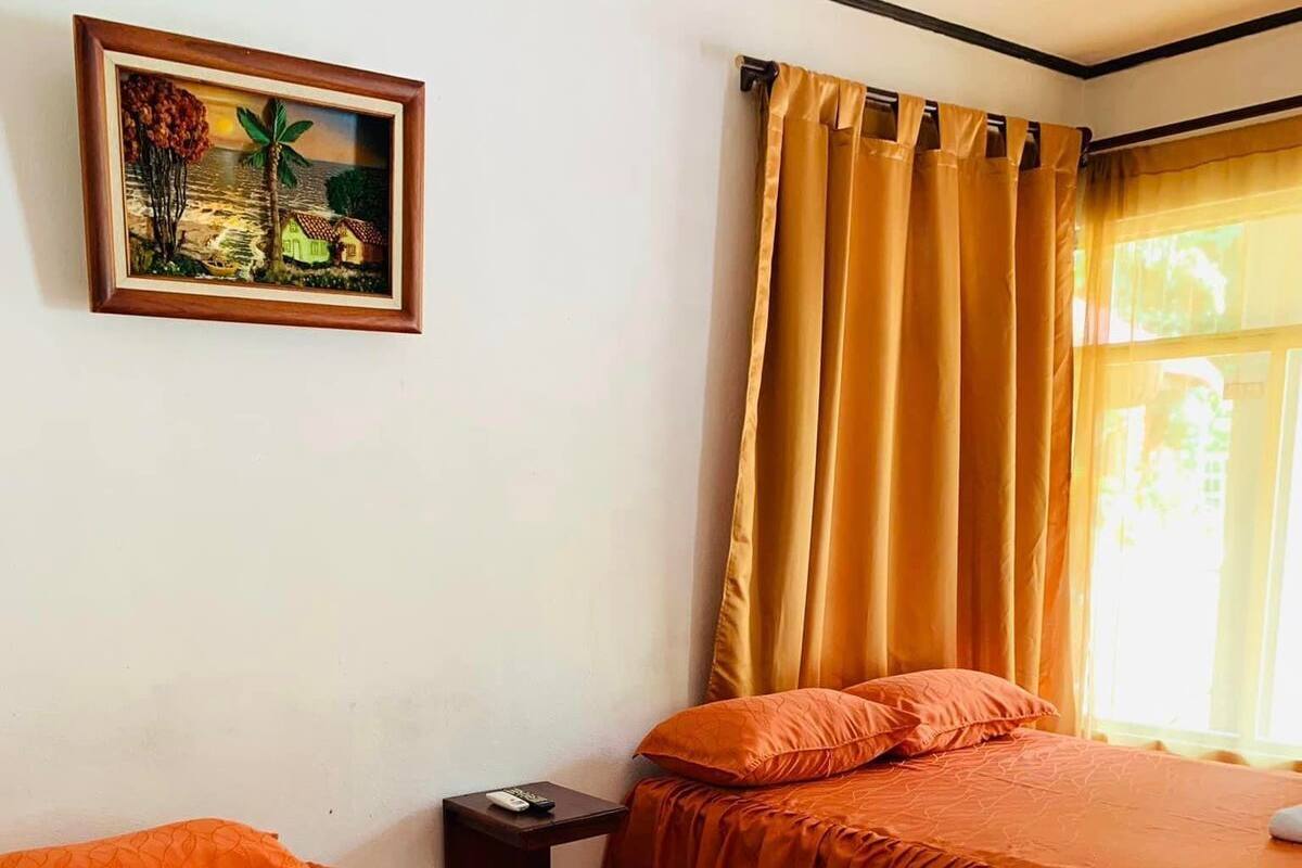 Een hotelkamer met twee bedden, oranje beddengoed, een schilderij aan de muur en een raam met gordijnen.