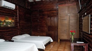 A rustic wooden room with two beds, a wooden wardrobe, a small table with a vase of flowers, and a painting on the wall. - Hotel Sun Sun Lodge (Horquetas)