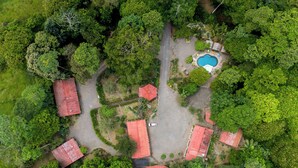 An aerial view of a property with multiple red-roofed buildings, a swimming pool, and lush greenery. - Hotel Sun Sun Lodge (Horquetas)