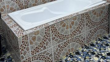 A bathroom with a rectangular bathtub, mosaic tile walls, and a window above the tub.