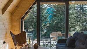 A cozy cabin interior with a large window, wooden walls, a sofa, a chair, and a small table. - Mountain Home Durmitor 1 (Uskoci)