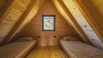 A small attic bedroom with two beds, a window, and wooden walls.