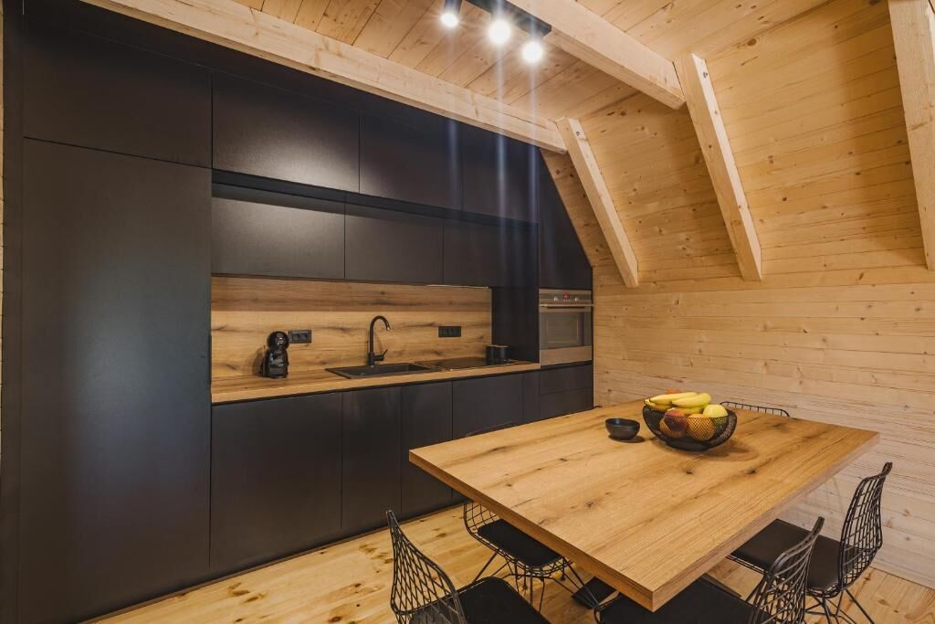 A modern kitchen with dark cabinetry, a wooden countertop, and a dining area with a wooden table and chairs.