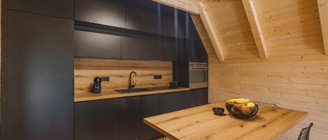A modern kitchen with dark cabinetry, a wooden countertop, and a dining area with a wooden table and chairs.