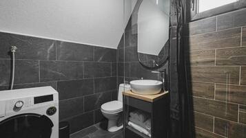 Een kleine badkamer met een wasmachine, toilet en een houten wastafelmeubel met spiegel.