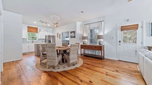 A modern kitchen with white cabinets, a dining area with wicker chairs, and a wooden floor.