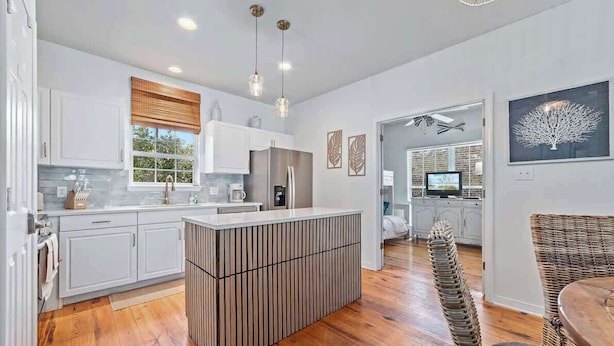 A modern kitchen with white cabinetry, a central island, and hanging pendant lights.