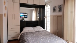 A bedroom with a bed, a wardrobe, a mirror, and artwork on the wall.