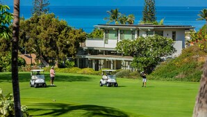 Campo de golf con vista al océano y un edificio moderno al fondo.