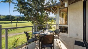 Un área de comedor al aire libre techada con una mesa dispuesta para cuatro personas, rodeada de sillas de mimbre, con vistas a un campo de golf con árboles y cielo despejado.