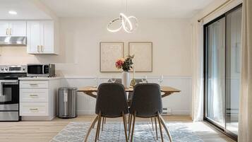 Una cocina moderna con armarios blancos, electrodomésticos de acero inoxidable y un comedor con mesa de madera y dos sillas.