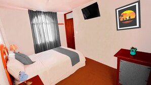 Ein Hotelzimmer mit einem Bett, einem kleinen Tisch mit einer Vase, einem an der Wand montierten Fernseher und einem gerahmten Bild einer Sonnenuntergangslandschaft.