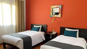 Ein Hotelzimmer mit zwei Betten, einem Nachttisch mit Telefon, einem an der Wand befestigten Spiegel und einem Fenster mit Vorhängen.