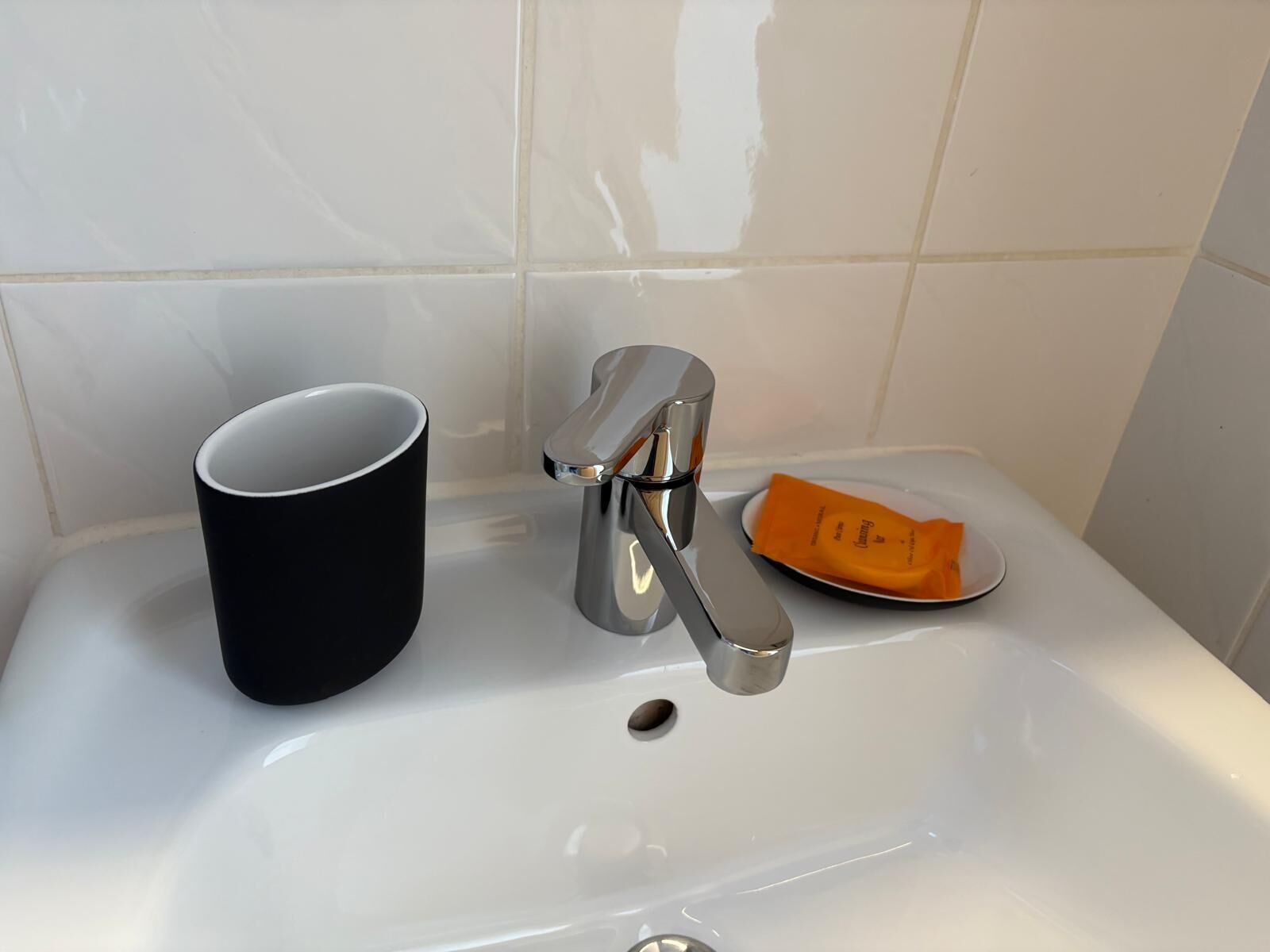 A bathroom sink with a black mug, a soap dish with a bar of soap, and a chrome faucet.