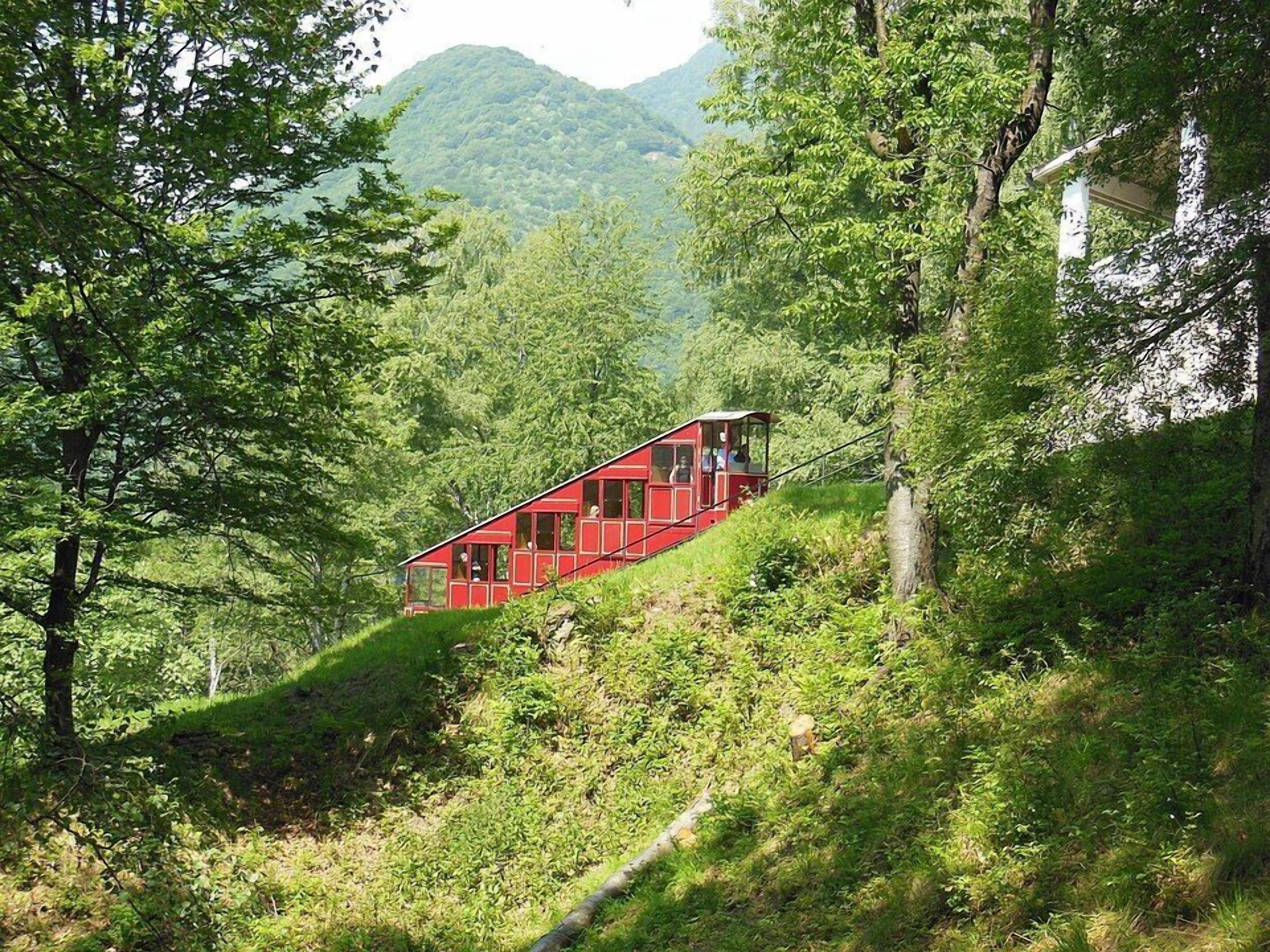 Una cabaña roja con múltiples ventanas, rodeada de abundante vegetación y una montaña al fondo.