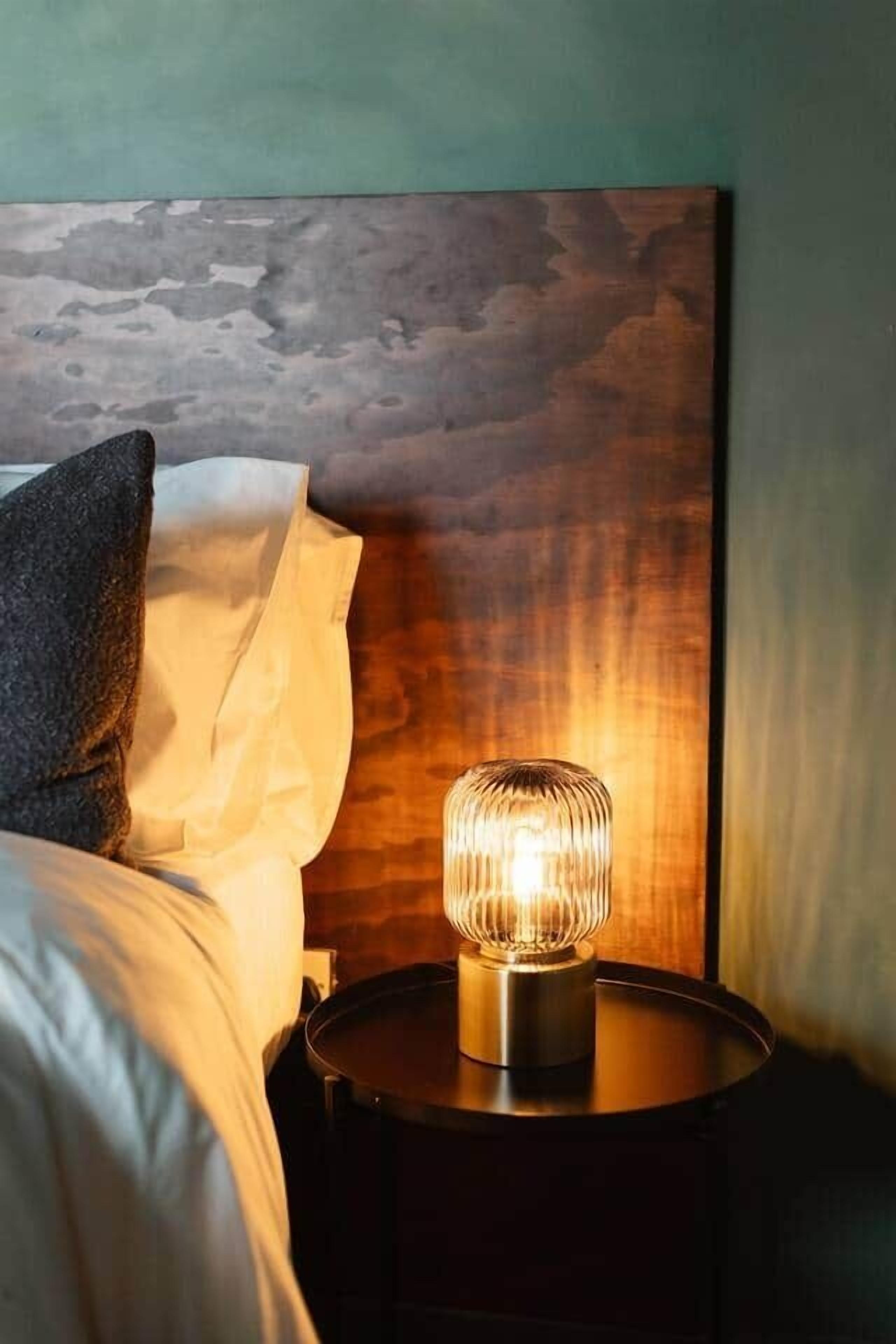 A bed with a pillow, a bedside table with a lamp, and a wooden headboard.