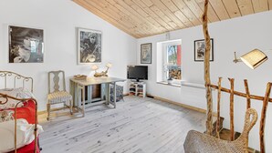 Ein Zimmer mit einem Bett, einem Sessel, einem Tisch mit Lampen, einem Fernseher und gerahmten Bildern an der Wand.