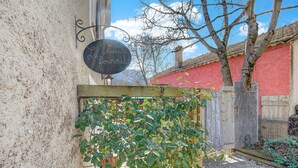 Ein Garten mit Holzzaun, einer Pergola mit Kletterpflanzen und einem Gebäude mit roter Wand und Schornstein.