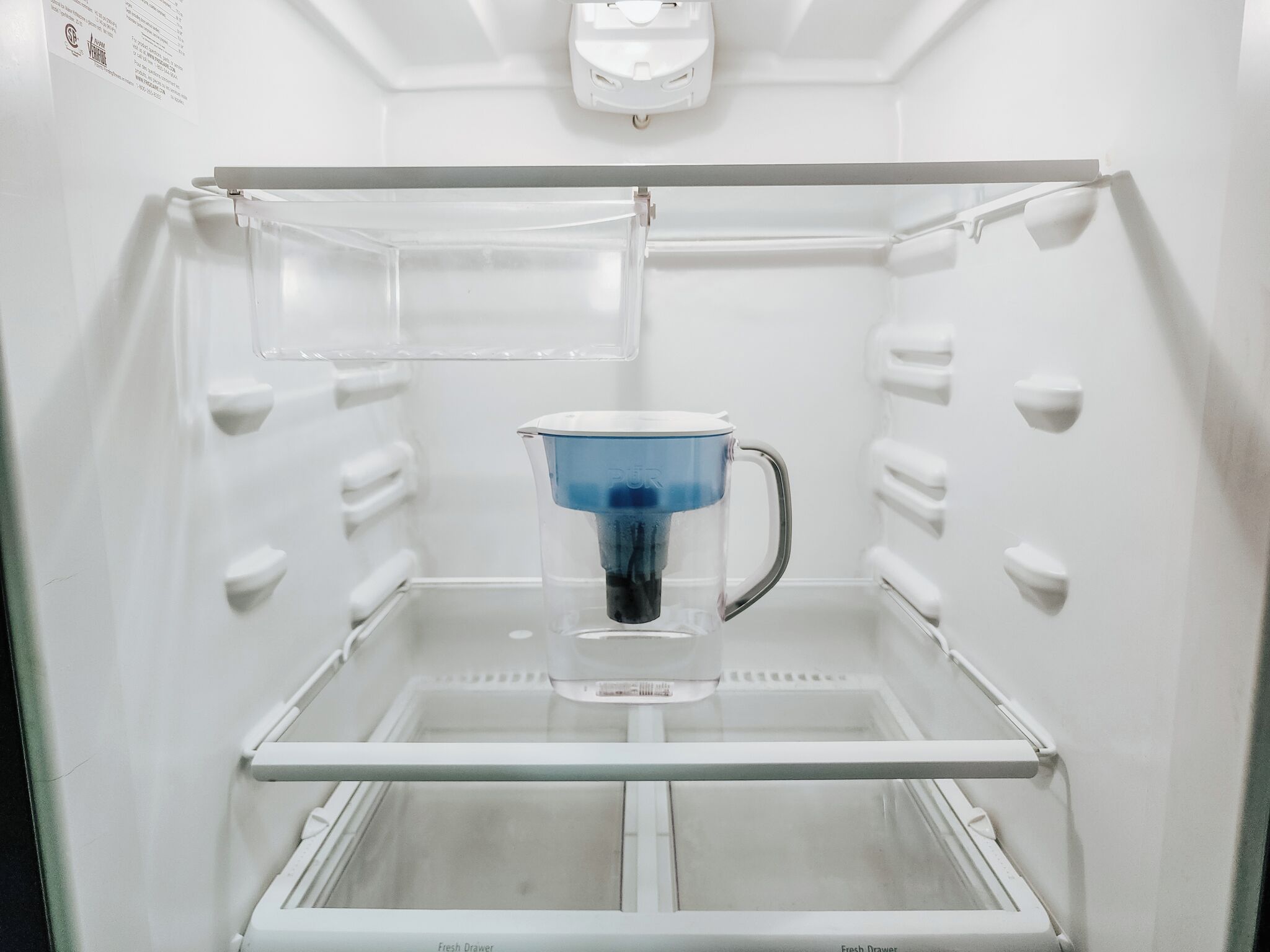 An empty refrigerator with a fresh drawer and a water dispenser.