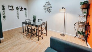 A modern living room with a glass-top dining table, dark wooden chairs, a blue sofa, a floor lamp, and a plant shelf. - Convention Cent / 2 King Beds / 65" TV / Fireplace (Philadelphia)
