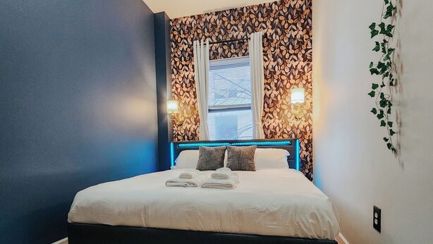 A modern bedroom with a bed, blue walls, and a window with curtains. - Convention Cent / 2 King Beds / 65" TV / Fireplace (Philadelphia)