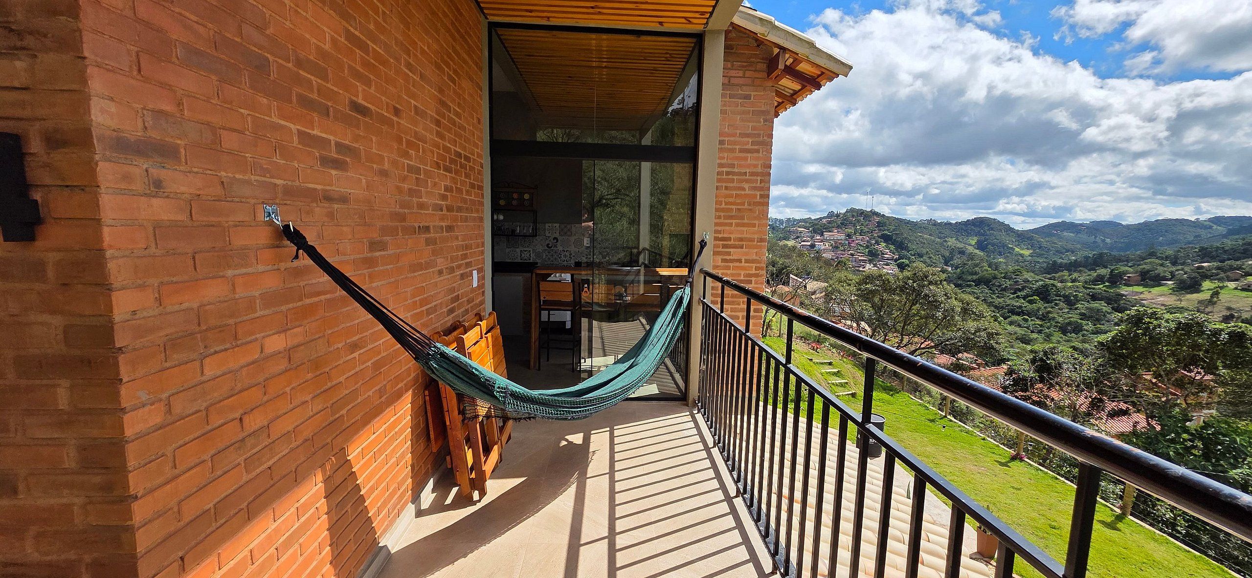 Un balcón con hamaca, paredes de ladrillo y vistas a un paisaje verde.
